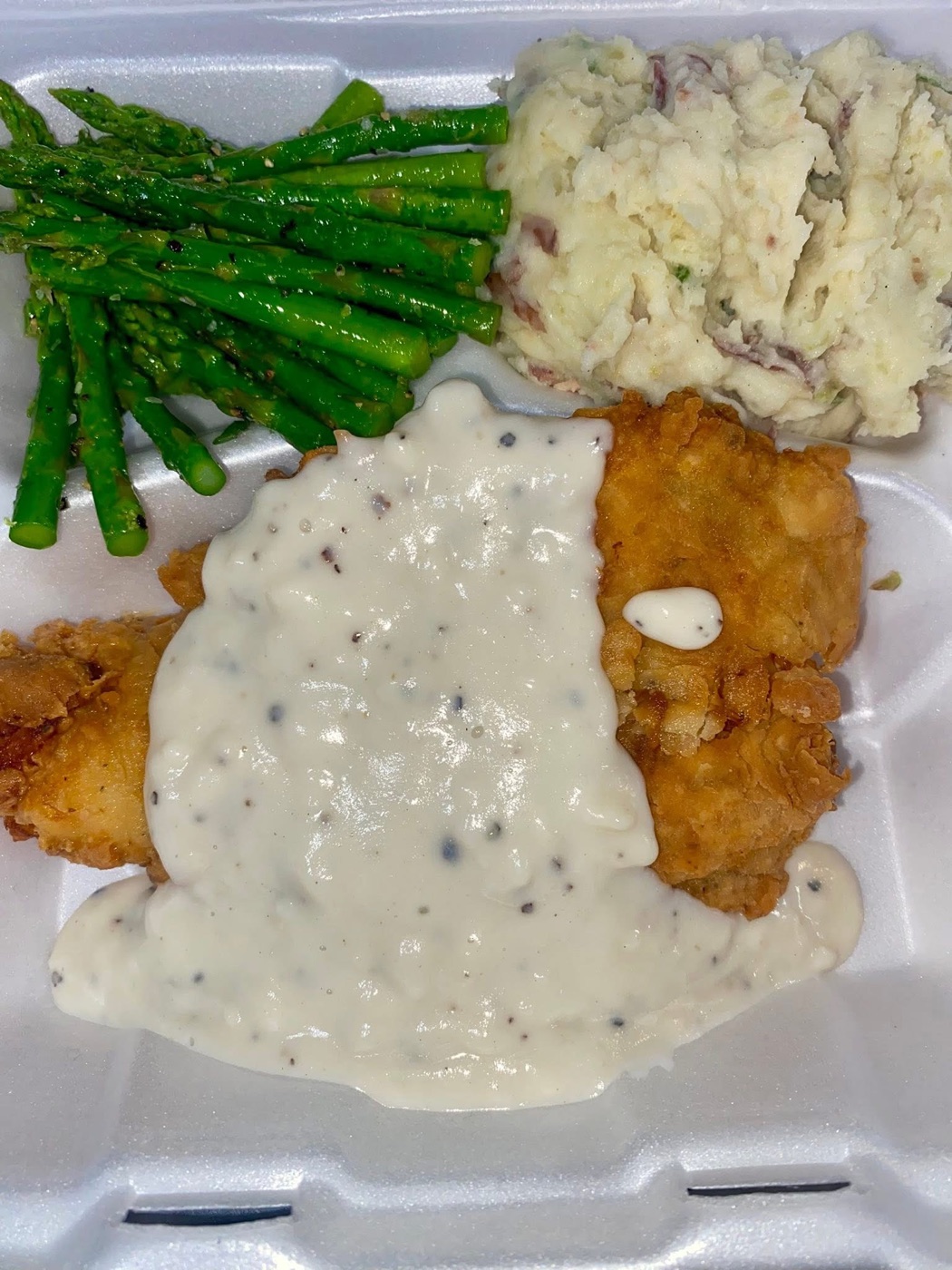 Fried chicken plated with pepper gravy, mashed potatoes and green beans