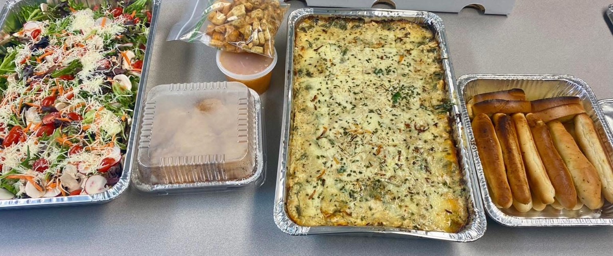 A catering line of salad, baked pasta and breadsticks in serving trays